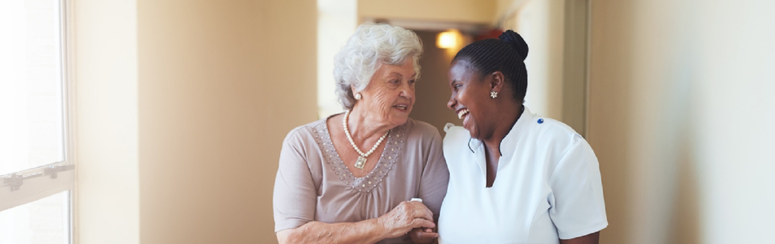 happy female caregiver and senior woman walking together