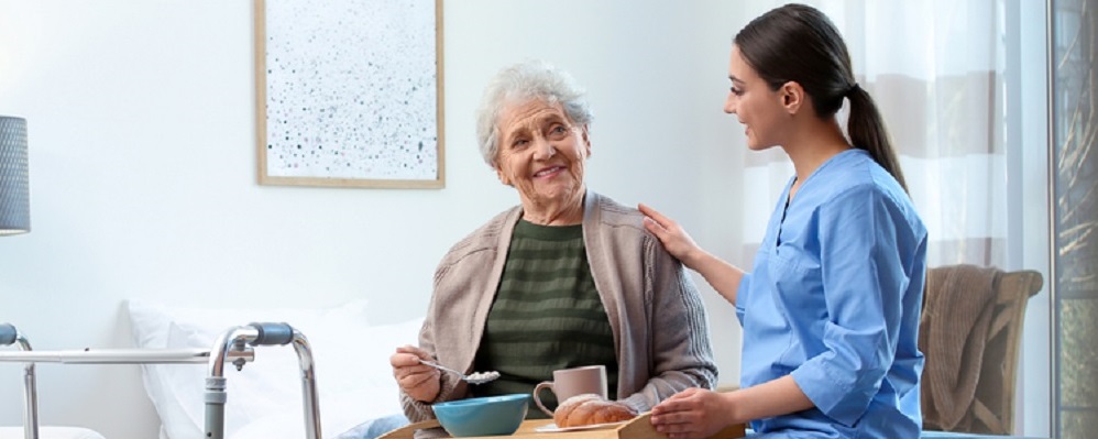 Care worker serving dinner for elderly woman on geriatric hospice