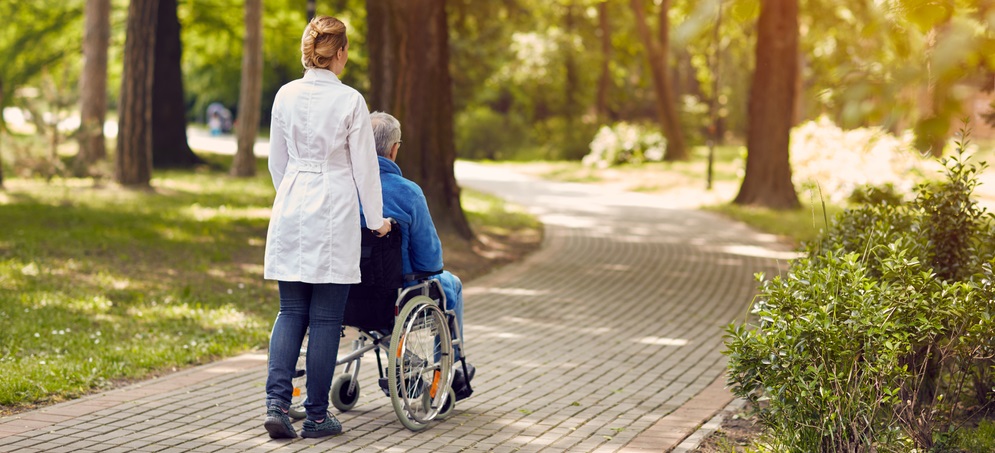 Hospice nurse helping elderly man on wheelchair outdoor
