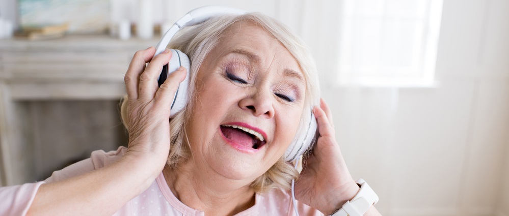 Happy senior woman with closed eyes wearing headphones and singing