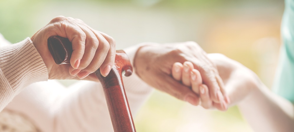 Closeup of senior lady holding walking stick in one hand and holding nurse's hand in the other